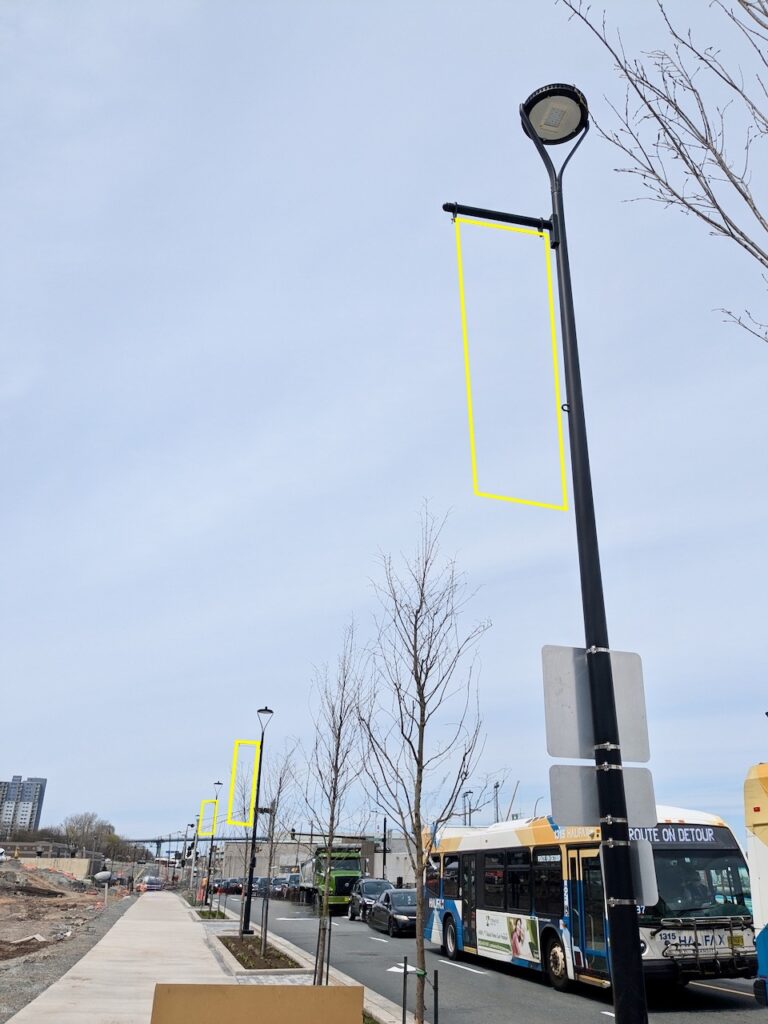 City street with lamp posts, bus, and busy traffic. Three vertical yellow rectangles have been digitally drawn over parallel to each lamp post, indicating where a banner would go.