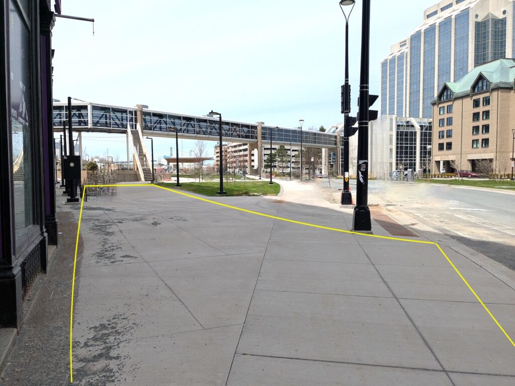 Photo of a city sidewalk next to a black building, with lightposts and a pedway stretching overhead. The sidewalk has been digitally drawn over the photograph to outline the visible sidewalk.